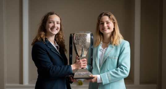 Female Oxford and Cambridge athletes holding the Women's Boat Race trophy